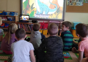 Dzieci oglądają film edukacyjny o dinozaurach na tablicy multimedialnej