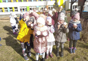 Dzieci pozują do zdjęcia w ogrodzie przedszkolnym trzymając w rękach znalezione jajka dinozaurów.