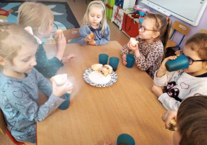 Dzieci siedzą przy stolikach, jedzą paczki i piją sok.