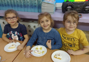 Dziewczynki siedzą uśmiechnięte przy stoliku z goframi na talerzach.