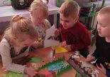 Dzieci siedzą przy stoliku tworząc elementy farmy z papieru