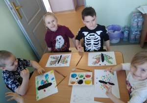 Dzieci przy stolikach malują palcami motyle