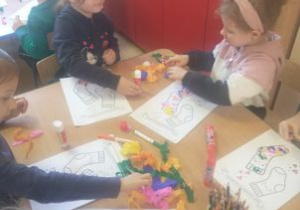 Dziewczynki przy stoliku ozdabiają rysunek skarpetki kulkami kolorowymi z bibuły
