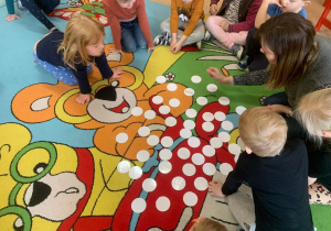 Dzieci siedzą na dywanie i grają w memory.