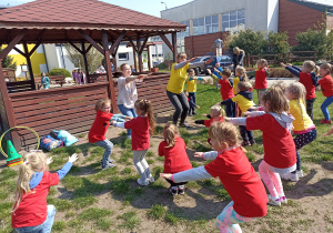 Dzieci wraz z nauczycielkami wykonują przysiady w ogródku przedszkolnym