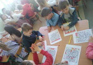 Dzieci przy stolikach wykonują pracę plastyczną - godło Polski