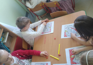 Dzieci przy stolikach wykonują pracę plastyczną - wyklejają plasteliną godło Polski