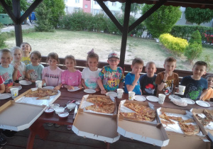Dzieci jedzą kolację w altanie przedszkolnej - cieszą się z zamówionych pizzy