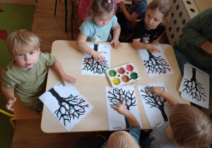 Dzieci malują farbami licie na jesiennym drzewie wykorzystując palce