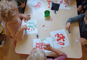Dzieci przy stolikach zapełniają kontury jabłka kolorowym papierem