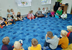 dzieci siedzą w kole na dywanie i odpowiadają na pytania pani bibliotekarki