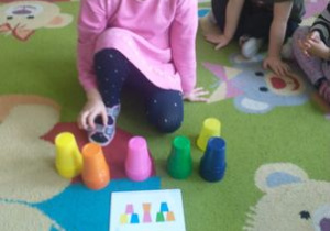 Dziewczynka układa kolorową wieże z kubeczków według wzoru.