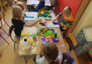 Dzieci wykonują pracę plastyczną przy stoliku.