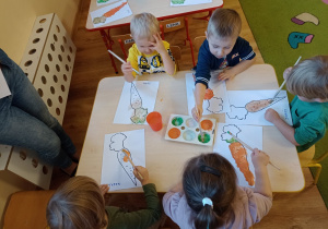 Dzieci wypełniają farbami kontury obrazka (marchewka)