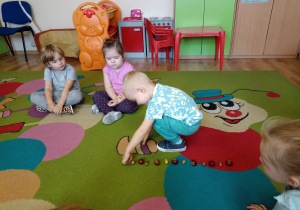 Chłopiec na dywanie układa dary jesieni: kasztany i żołędzie według ustalonego rytmu