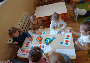 Dzieci przy stolikach układają figury geometryczne według podanego rytmu