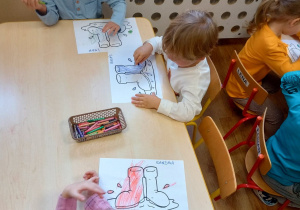 Dzieci przy stolikach wypełniają kredkami kontury kaloszy