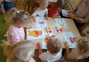 Dzieci przy stolikach malują postać Kubusia Puchatka