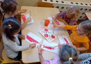Dzieci przy stolikach malują farbami flagę Polski