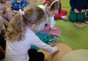 Dzieci segregują na dywanie kredki według koloru i wielkości