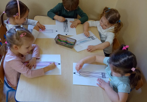Dzieci przy stolikach zapełniają kontury obrazka kredkami