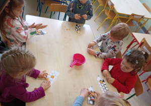 dzieci przy stolikach w skupieniu wyklejają kredki plasteliną