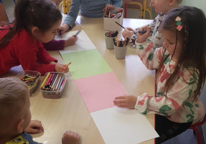 dzieci przy stolikach malują kredkę z papieru