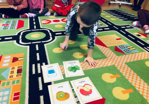 Chłopiec podchodzi do leżących na dywanie kart.