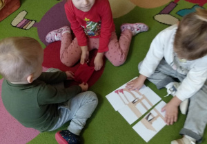 Dzieci w grupach układają puzzle - pocięty na trzy części obrazek przedstawiający sanki