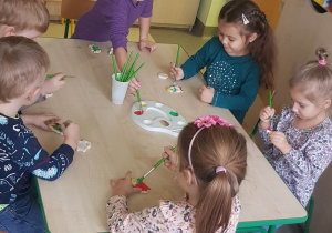 dzieci siedzą przy stoliku, malują farbami figurki z masy solnej