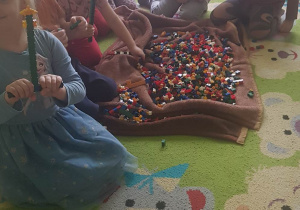 dzieci siedzą na dywanie, bawią się klockami, budują konstrukcje