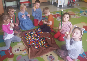 dzieci siedzą na dywanie, pokazują zbudowane konstrukcje z klocków