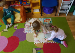 Dzieci układają piankowe puzzle na dywanie