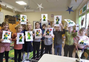Dzieci stoją trzymając w górze swoje prace z postacią Franklina.