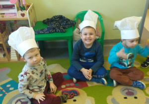 dzieci siedzą na dywanie, na głowie mają czapki kucharskie