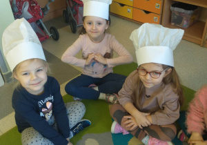 dzieci siedzą na dywanie, na głowie mają czapki kucharskie