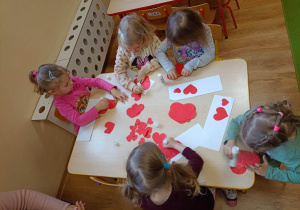 Dziewczynki przyklejają na kartkę papierowe serca od największego do najmniejszego