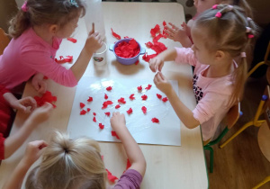 Dziewczynki wypełniają kontury serca bibułą - praca w grupie przy stoliku