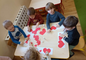 Chłopcy przyklejają na kartkę papierowe serca od największego do najmniejszego