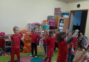 Dzieci ubrane w stroje w czerwonym kolorze wykonują ćwiczenia gimnastyczne