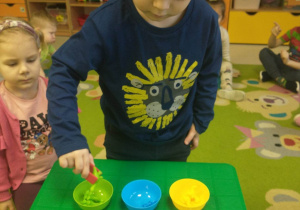chłopiec stoi na dywanie, chłopiec układa sekwencje- kolorowe dinozaury