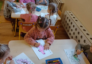 Dzieci wypełniają kredkami i plasteliną rysunek konturowy dinozaura