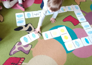 Dzieci układają domino z symbolami pogodowymi na dywanie