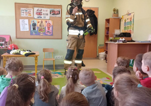 Strażak prezentuje się dzieciom w specjalnym stroju przeznaczonym go gaszenia pożaru