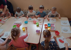 Dzieci kolorowymi lukrami malują jajko-wielkanocną pisankę