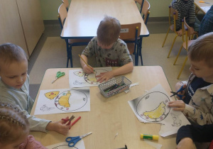 dzieci malują, wycinają nożyczkami kurczaczka przy stoliku