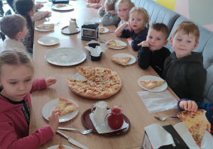 dzieci przy stole jedzą pizze