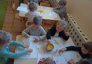 Dzieci tworzą kurczaczka wielkanocnego wykorzystując pociętą żółtą bibułę