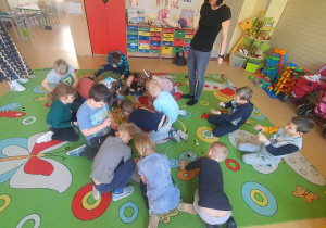 Dzieci na dywanie wykonują ćwiczenia logopedyczne.