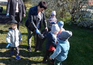 Dzieci wrzucają znalezione w ogródku przedszkolnym śmieci do kosza